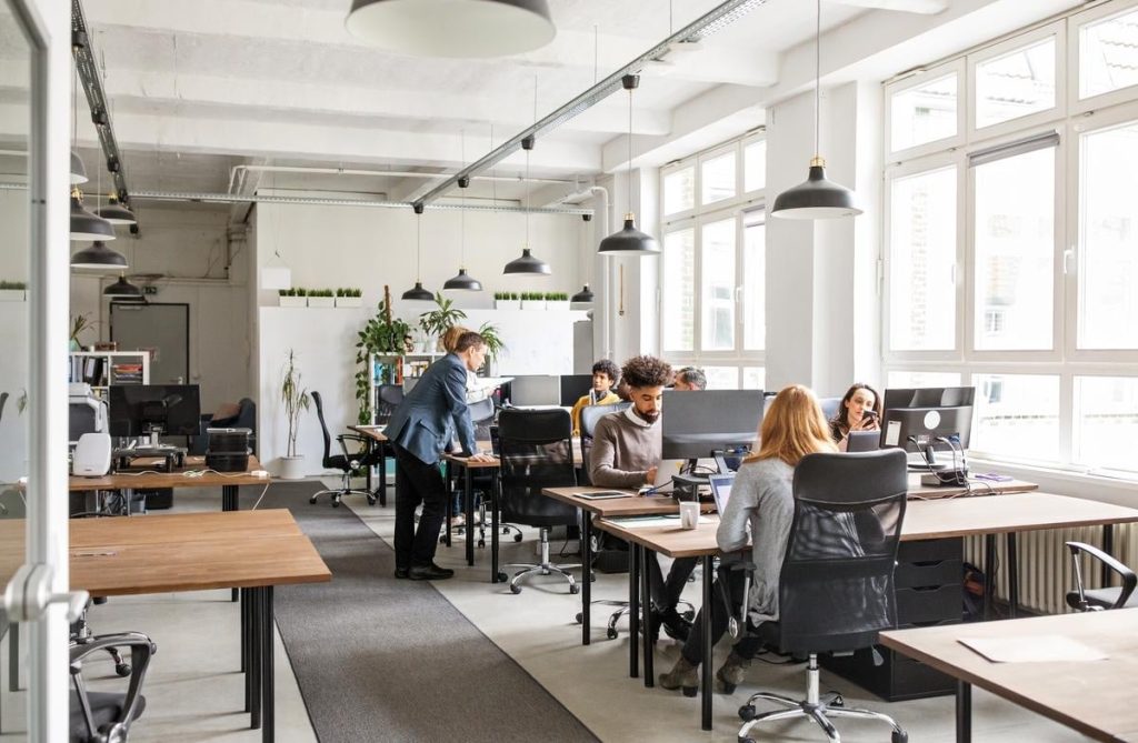 An office full of workers by their monitors or chatting with each other
