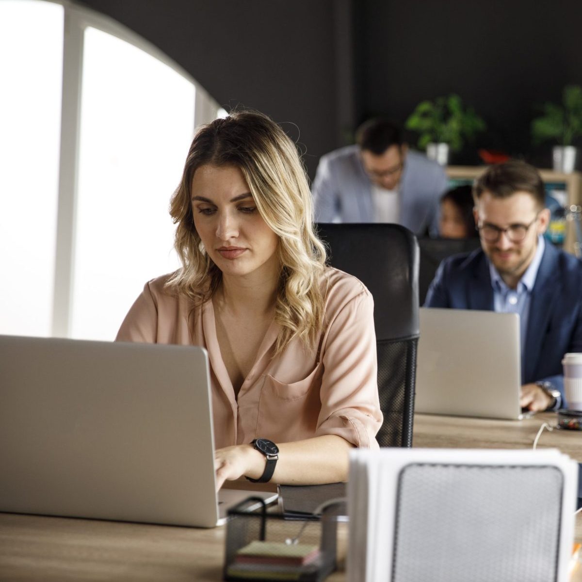 Selective focus shot of group of business people sitting in a row, at their desk at the office, using laptop and working diligently.